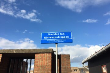 Straatnaambordje Graodus fan Nimwegentrappen. Met onderschrift waarop staat dat Graodus fan Nimwegen de bijnaam was van Theo Eikmans (1921-2000), Nijmeegse zanger en tonprater.